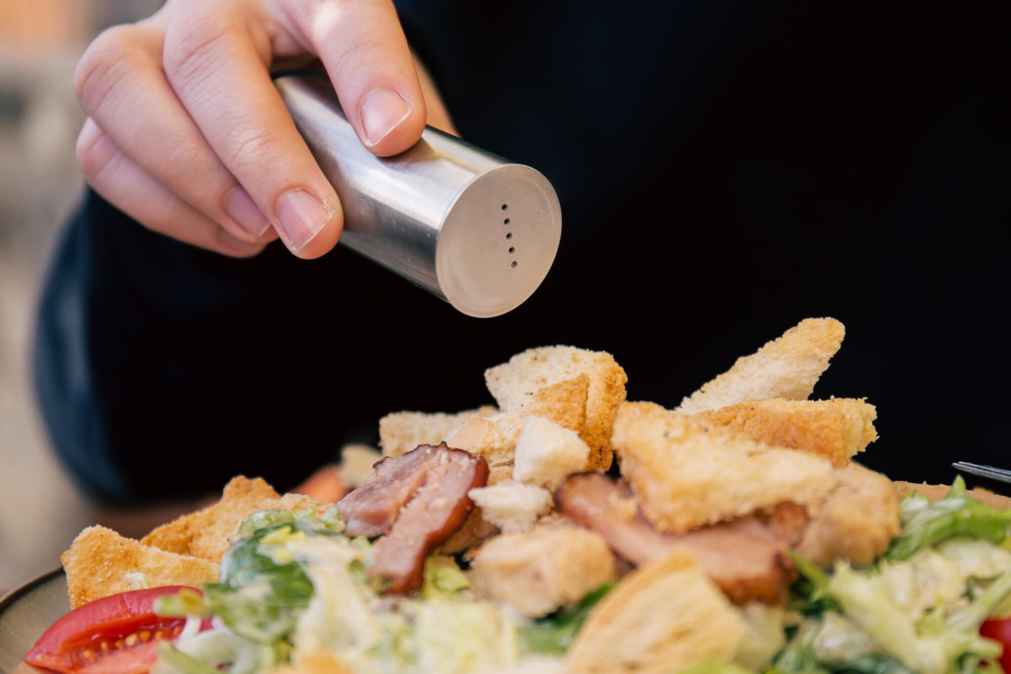 closeup man pours pepper into salad