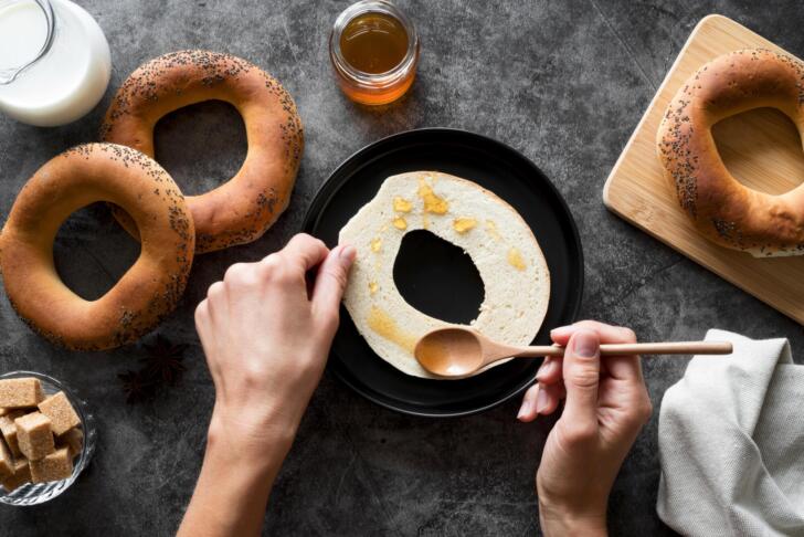 flat lay hand spreading honey sliced bagel
